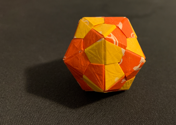 a modular origami icosahedron built from orange and yellow starburst wrappers